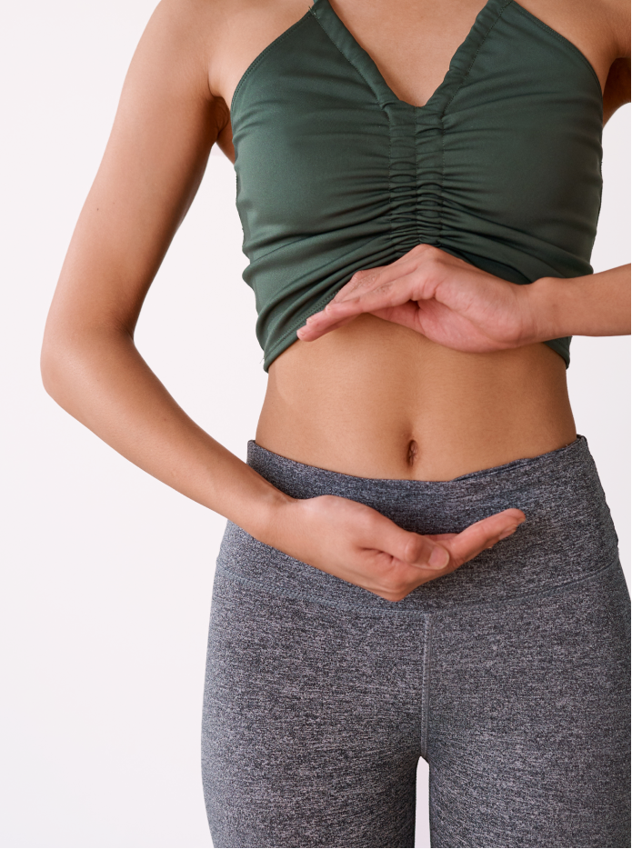 A woman standing with her hands resting on her lower abdomen.